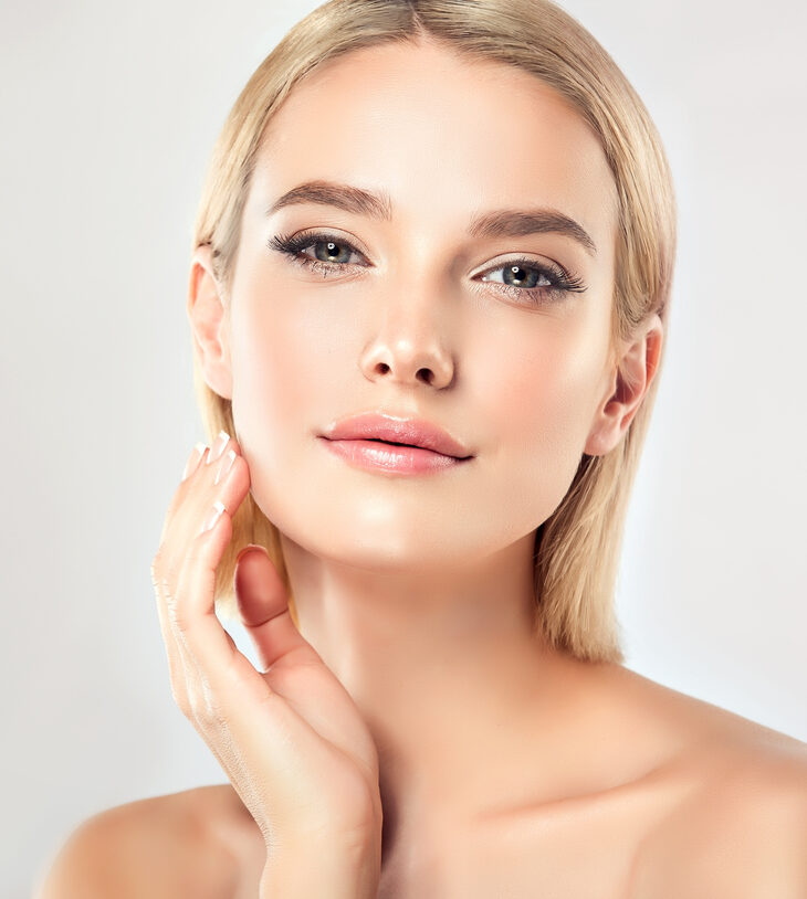 Gorgeous, young,woman with almond like eyes is touching tenderly the face. Facial treatment, cosmetology and spa.