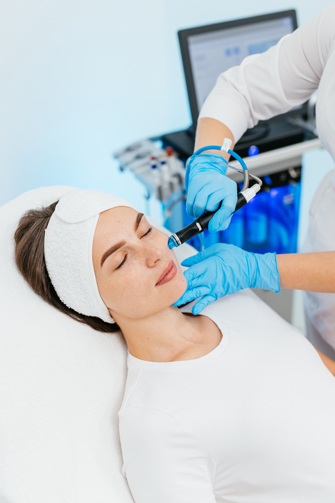 Young woman is relaxing getting vaccum facial hydro peeling procedure in beauty salon. Hardware face pores cleansing, close-up.